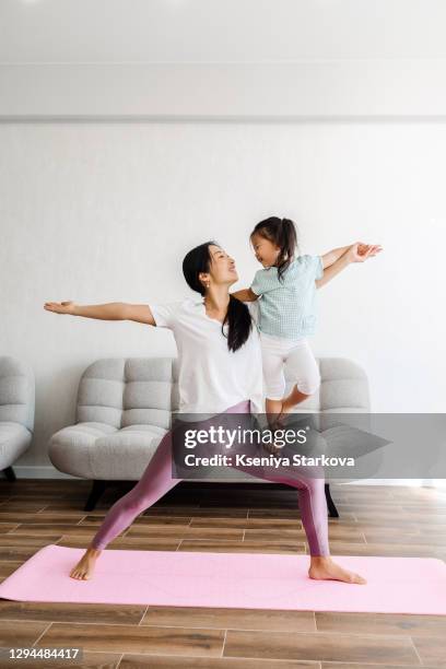 young asian mom and her daughter doing yoga in the living room - pro russian stock pictures, royalty-free photos & images