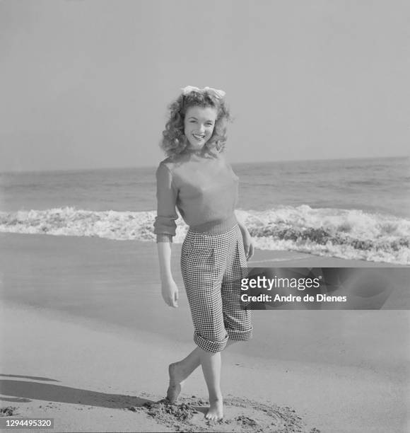 Portrait of American actress and model Marilyn Monroe in a sweater and checkered trousers, as she poses at Zuma Beach's Paradise Cove, California,...