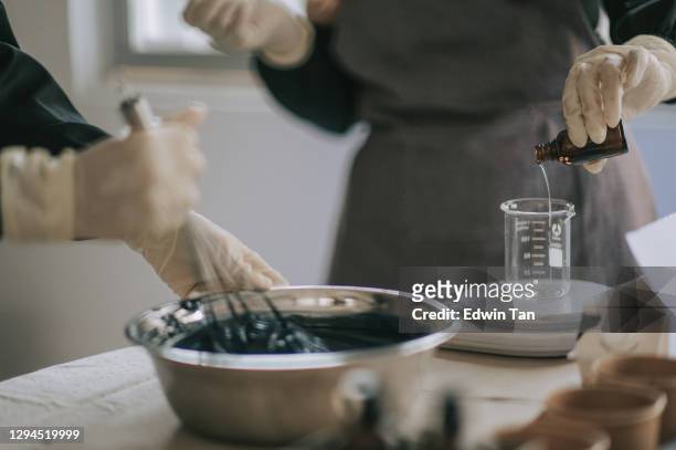 close up hands of asian chinese teenage boy stirring raw material gel liquid and female craftperson pouring essential oil into measuring glass - homemade soap stock pictures, royalty-free photos & images