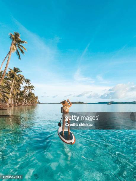 mujer disfrutando de stand up paddle boarding en los trópicos - idílico fotografías e imágenes de stock