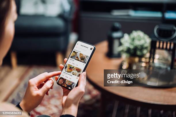 close up of young asian woman using meal delivery service and ordering food online with mobile app on smartphone while sitting on the sofa in the living room at a cozy home - buying lunch stock-fotos und bilder