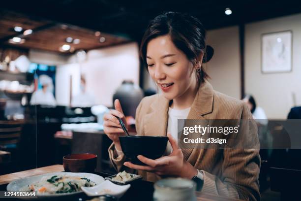 smiling young asian woman enjoying freshly served traditional japanese cuisine with assorted side dishes, miso soup and green tea in a japanese restaurant - chinese soup photos et images de collection