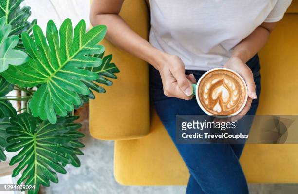 enjoying fresh coffee. top view of beautiful young woman holding cup while relaxing on sofa at home - enjoying coffee cafe morning light stock-fotos und bilder