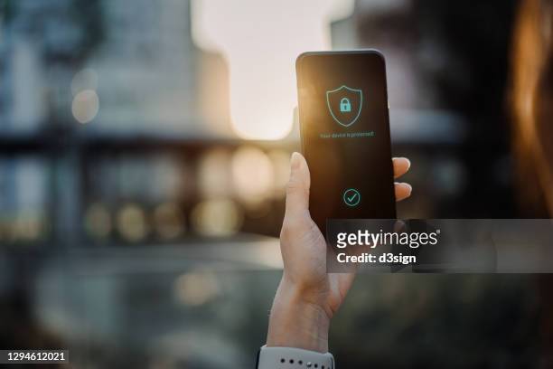close up of young woman using smartphone in downtown district in the city against urban city scene, with a security key lock icon on the smartphone screen. privacy protection, internet and mobile security concept - beveiliging stockfoto's en -beelden