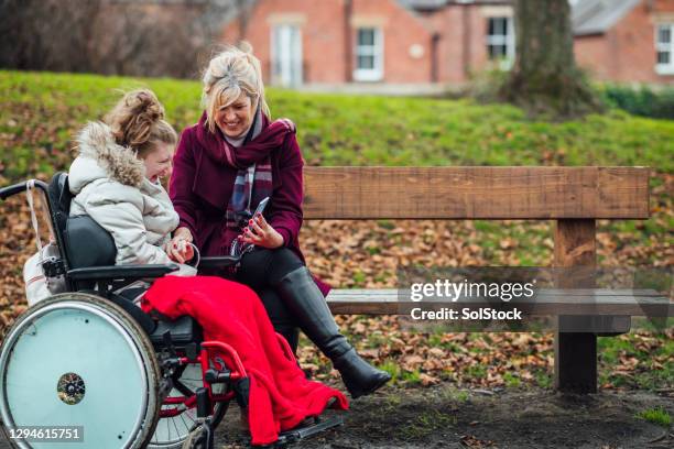 mãe e filha usando telefone inteligente em um banco de parque - esclerose lateral amiotrófica - fotografias e filmes do acervo