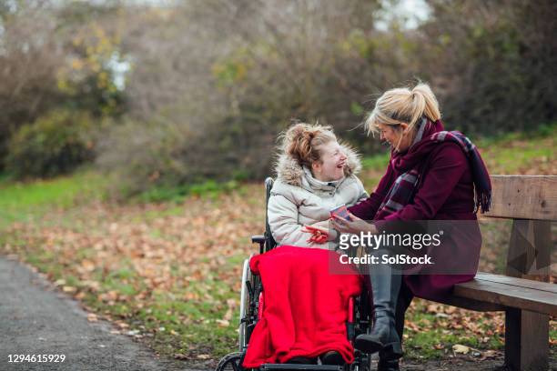 moeder en dochter die slimme telefoon in openbaar park gebruiken - disability care stockfoto's en -beelden