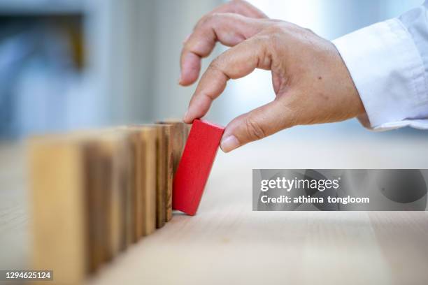 man hand pick up a red wooden blocks.wooden blocks and the effect of dominoes. - washinton dc premiere of national geographics chain of command stockfoto's en -beelden