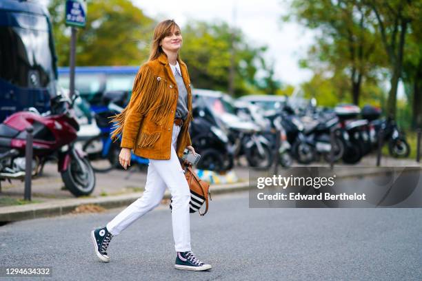 Guest wears a brown suede fringed jacket, a gray wool pullover with white lace collar, a brown leather belt, white pants, Converse ankle sneakers...