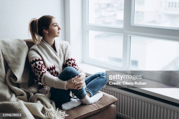 portrait of a woman in a white sweater and jeans looks out the window - woman wearing white jeans ストックフォトと画像