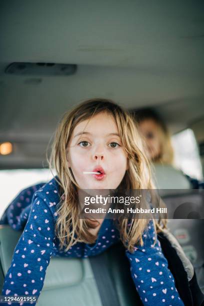 young girl in back of car with lollipop and silly face looks at camera - lollipops stock-fotos und bilder