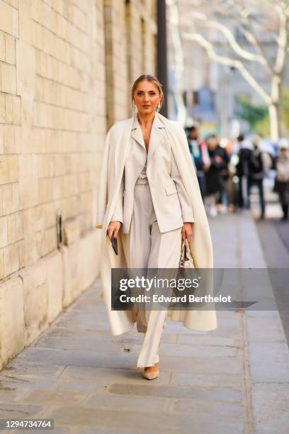 Guest wears earrings, a beige pantsuit, a cream-color coat, a ring, a brown and white crocodile handbag, beige suede pointy pumps, outside Dior,...