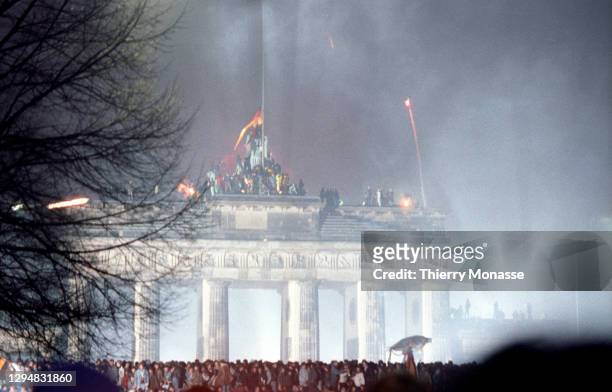 Revelers at the Brandenburg Gate stand on top of a remnant of the Berlin Wall, as they celebrate the first New Year in a unified Berlin since World...