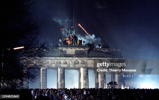 Revelers at the Brandenburg Gate stand on top of a remnant of the Berlin Wall, as they celebrate the first New Year in a unified Berlin since World...