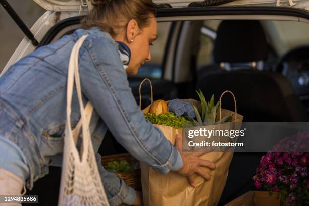 mature woman loading shopping bags in a car trunk - textile for delivery stock pictures, royalty-free photos & images