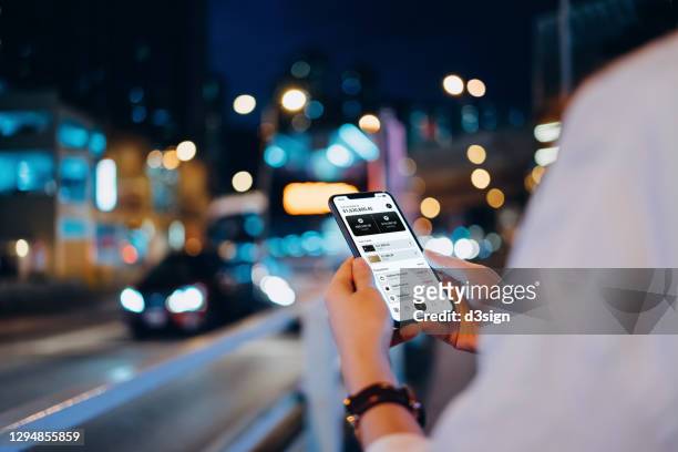 close up of young asian woman managing online banking with mobile app on smartphone on the go. transferring money, paying bills, checking balance in downtown city street against illuminated city buildings and traffic by the urban road at night - downtown shopping stock pictures, royalty-free photos & images