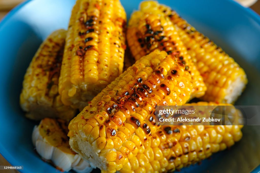 The cobs of yellow corn roasted on the grill, sprinkled with spices on the vibrant ceramic plate. The concept of cooking homemade food.