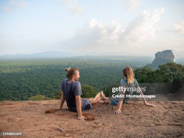 rear view of young couple sitting on top of rock at sunset contemplating the beautiful jungle natural landscape - rainy season stock pictures, royalty-free photos & images