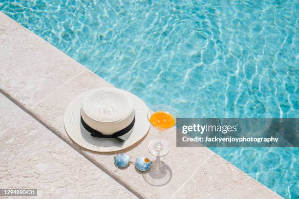 fresh drink an orange juice, hat and glasses on the floor in front of pool in background in koh samui. summer concept - beach hotel imagens e fotografias de stock