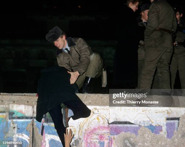 East Deutsche Volkspolizei helps a woman to climb on the Berlin wall during the New-Year Eve on December 31, 1989 in Berlin, Germany.