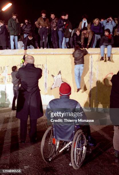 Disabled man in a wheelchair is lloking at man who are climbing on the Berlin Wall near by the Brandenburg Gate, as they celebrate the first New Year...