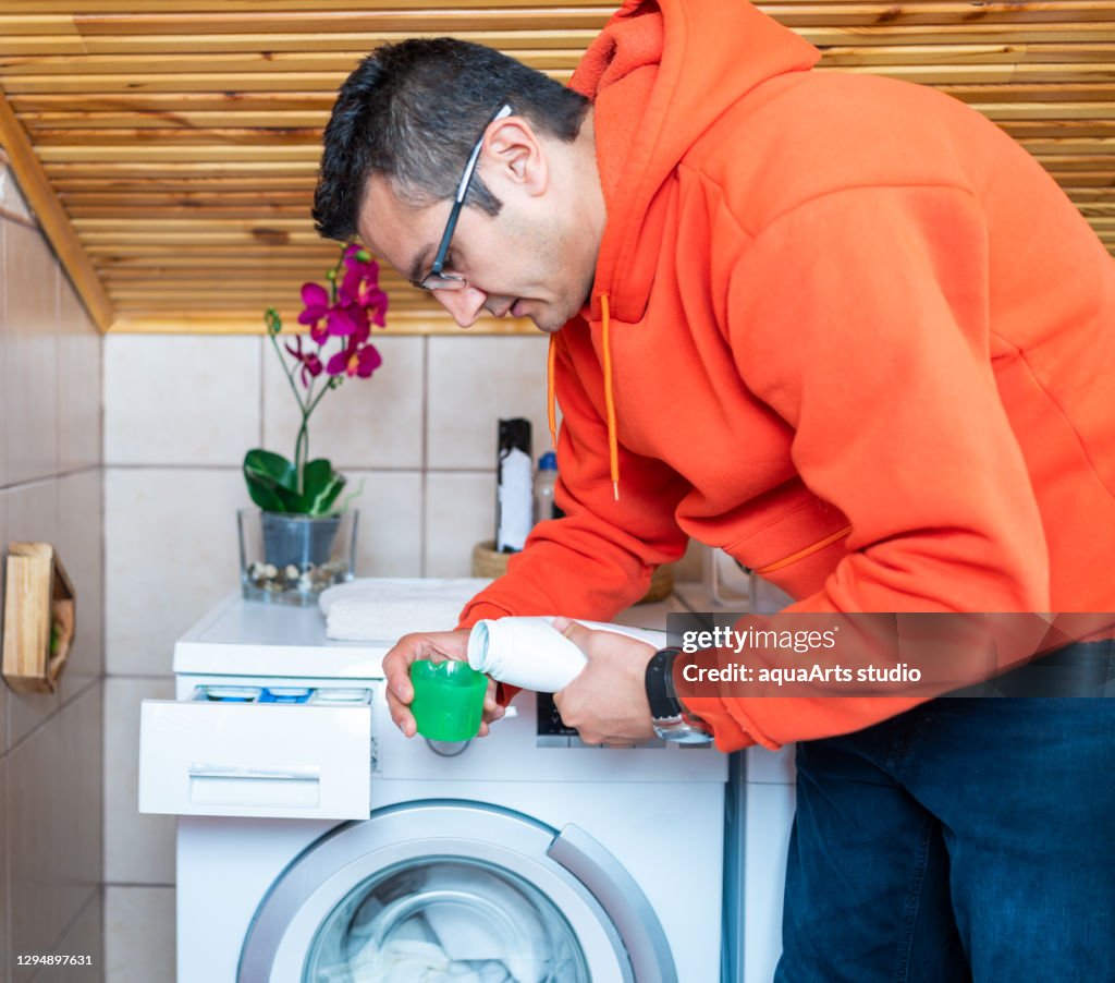 Junger Mann legt Waschmittel in Waschmaschine. Wäschetag