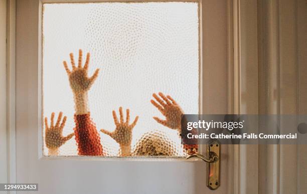 conceptual image of hands pressed against a glass window in an old interior door - key in door stock-fotos und bilder