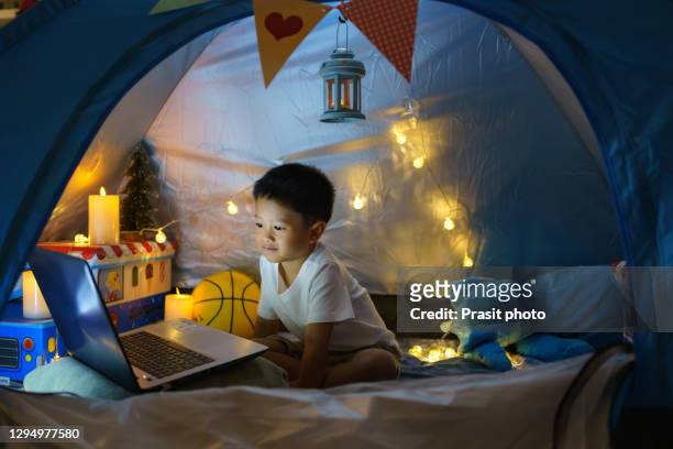 asian preschool boy child to make a camp to play imaginatively with light ball and candle and watching a film on laptop in the darkness of the camp in living room at home. - film lighting equipment stock pictures, royalty-free photos & images