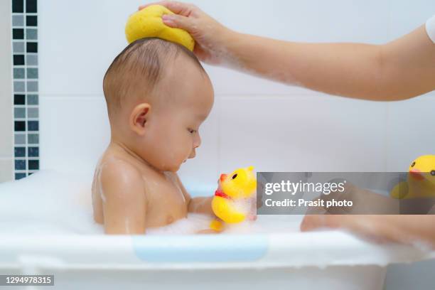 asian baby girl bathing in the white bathtub with her mother with smiling and playing yellow duck full of happiness in bathroom at home - baby shower - fotografias e filmes do acervo