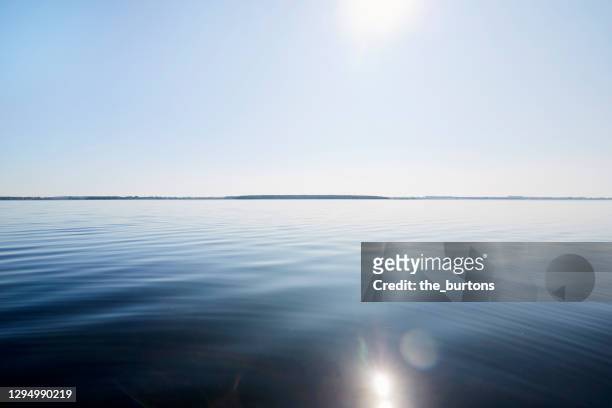 full frame shot of smooth sea and blue sky against sun - glatte oberfläche stock-fotos und bilder