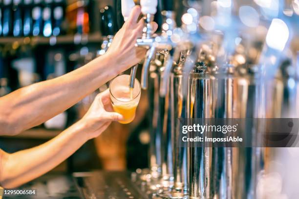 male hands poured beer from the tap. pouring beer for client. side view of young bartender pouring beer while standing at the bar counter. - beer alcohol stockfoto's en -beelden