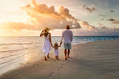 A family walks hand in hand down a tropical paradise beach during sunset