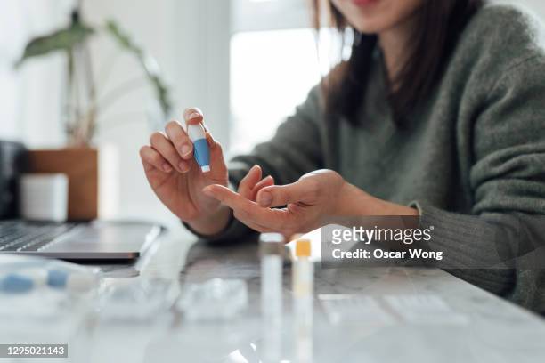 cropped shot of young woman doing finger-prink blood test at home - diabetic stockfoto's en -beelden