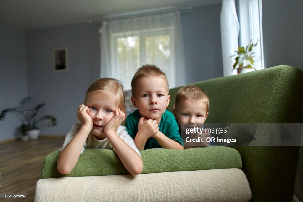 Portrait of triplet siblings lying on couch at home