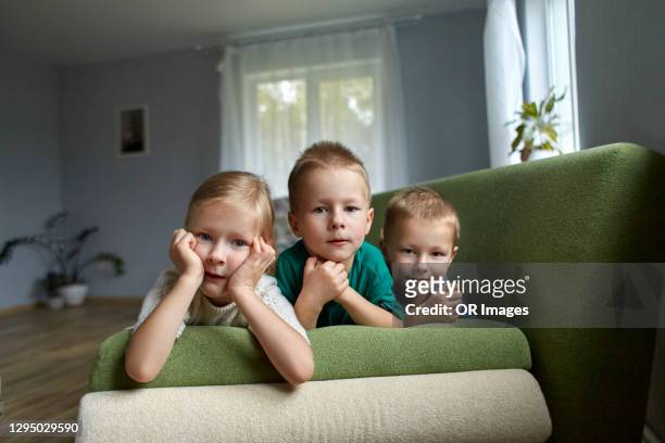 portrait of triplet siblings lying on couch at home - triplet stock pictures, royalty-free photos & images
