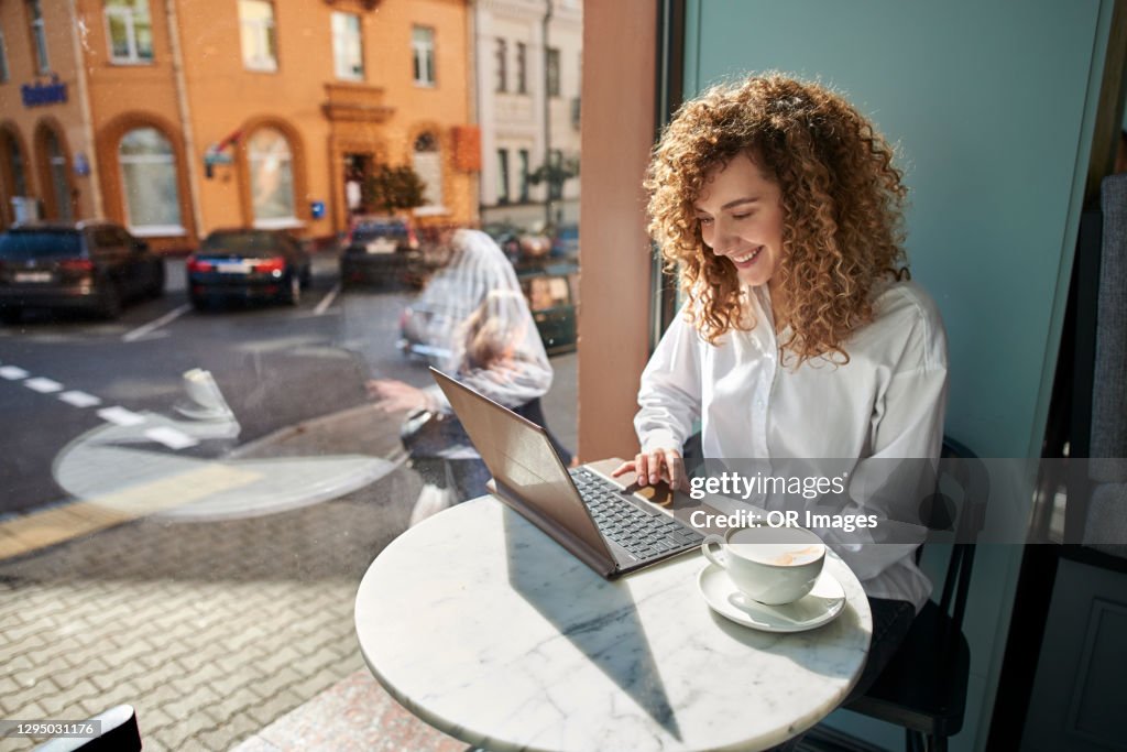 Smiling young woman using laptop in a cafe