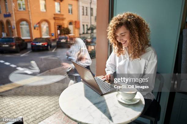 smiling young woman using laptop in a cafe - coffee window stock pictures, royalty-free photos & images
