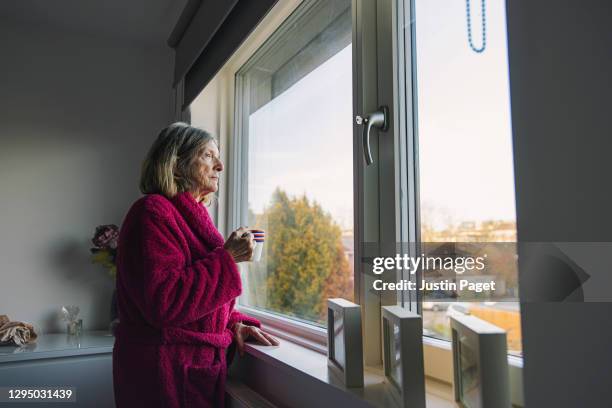 sad senior woman looking out of the window - loneliness stock pictures, royalty-free photos & images