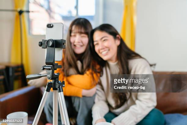 2人の若い女性の友人が自宅でスマートフォンでソーシャルメディアでライブストリーミング - tripod ストックフォトと画像