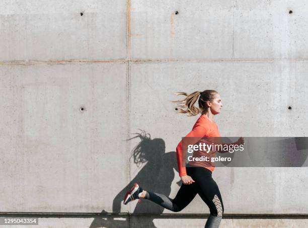 joven deportista corriendo frente a la pared de hormigón - corredora de footing fotografías e imágenes de stock