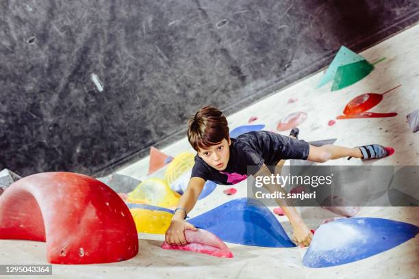 ragazzo che scala una parete da arrampicata interna - arrampicata sui boulder foto e immagini stock