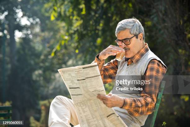 senior man drinking tea and reading newspaper at park bench - topnews stock pictures, royalty-free photos & images