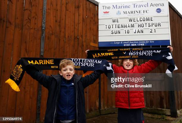 Two local young Marine FC fans pose for a photograph with their match day scarves in front of the clubs board displaying their next home game the FA...