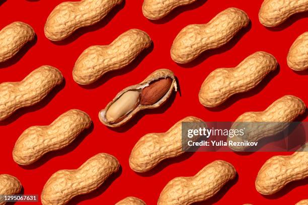 repeated peanuts ad one halved nut on the red background - peanut shell stock pictures, royalty-free photos & images