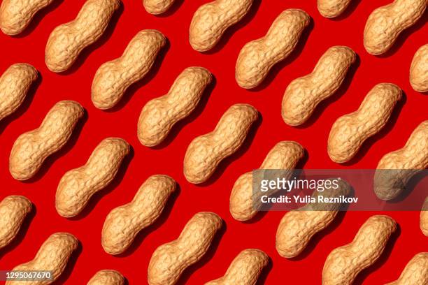 repeated nuts on the red background - erdnuss stock-fotos und bilder