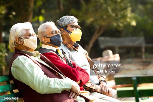 senior men wearing face masks while relaxing at park - protective face mask stock pictures, royalty-free photos & images