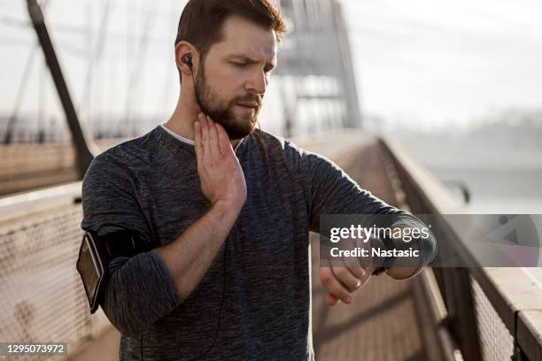 young athlete runner in headphones looks at a smart watch holding carotid with fingers - taking pulse stock pictures, royalty-free photos & images