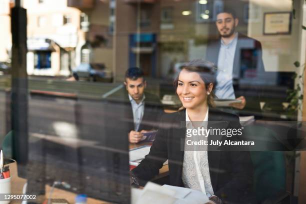 group of happy workers behind a window looking at computer from their office - bank office clerks stock pictures, royalty-free photos & images