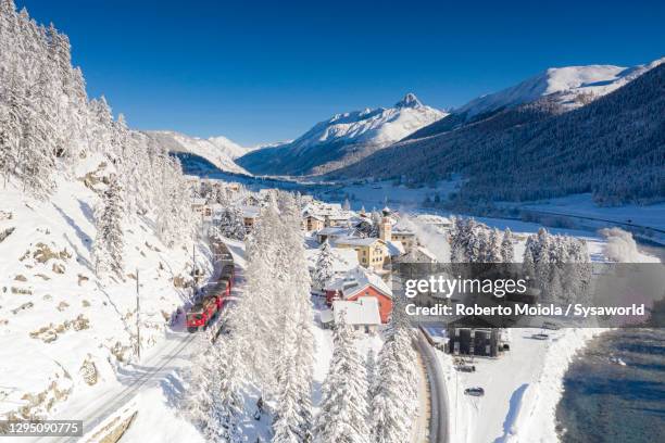 bernina express train in the snow beside inn river, switzerland - st moritz stock-fotos und bilder