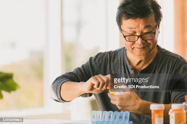 retired man sorts medication into pill organizer - medicine bottle stock pictures, royalty-free photos & images