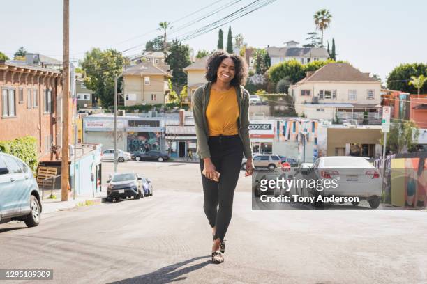 young woman holding phone walking on street - a la moda stock pictures, royalty-free photos & images